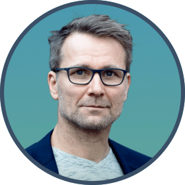 Porträt von Steffen Böye mit Brille und Dreitagebart vor blauem Hintergrund, Kommunikationstrainer bei Out of the Box Training.